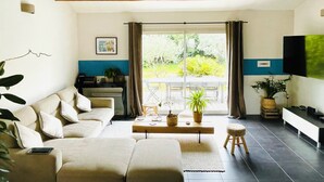 Ein Wohnzimmer mit einer Couch, einem Couchtisch, einem Fernseher und einer Glastür zum Balkon.