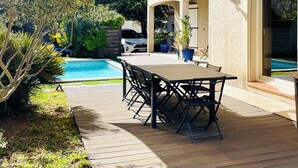 Eine Terrasse mit Tisch und Stühlen, ein Schwimmbad und ein Haus mit einem Ziegeldach.
