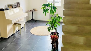Ein Wohnzimmer mit einem Klavier, einer Treppe, einer Topfpflanze und einer gewebten Leuchte.