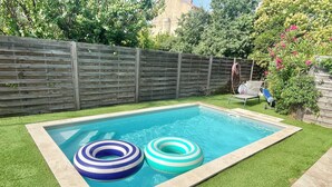 Ein rechteckiger Swimmingpool mit zwei Luftreifen, umgeben von Kunstgrün und einem Holzzaun.
