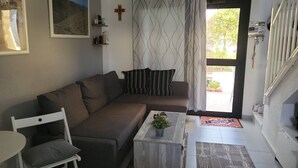 Ett vardagsrum med en soffa, ett litet bord med en växt, ett kors på väggen och en trappa som leder upp till en övre våning.
