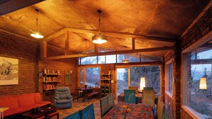 Una habitación acogedora con techo de madera, un ventanal grande, un banco acolchado y una estantería.