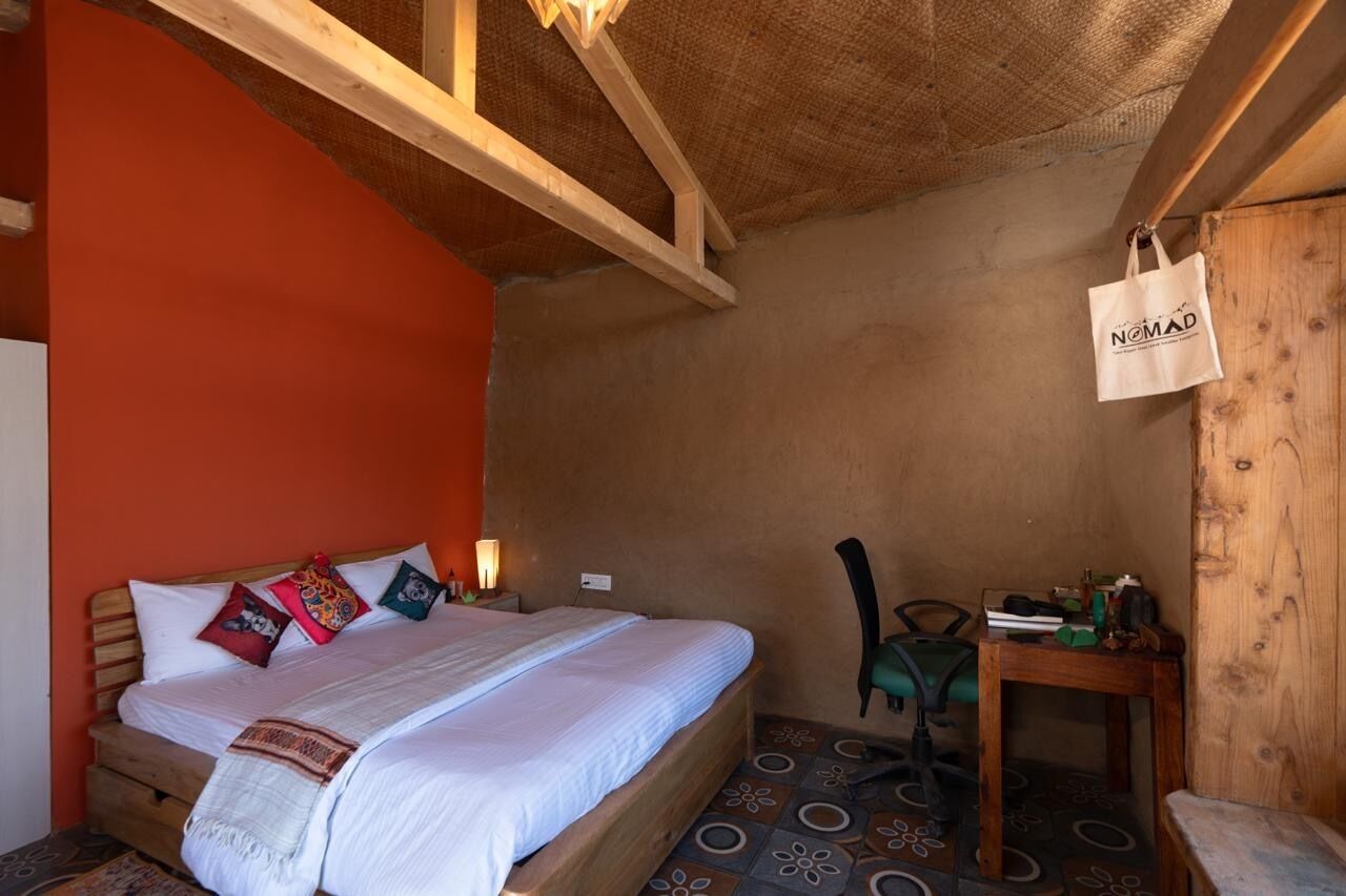 A bedroom with a wooden bed, a nightstand, a chair, a small table, and a wall-mounted bag.