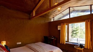 Una habitación con una cama, una mesita, una silla y un ventanal con cortinas.