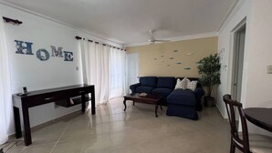 A living room with a sofa, a coffee table, a TV stand, and a dining area with a table and chairs. - Garden Condos 48 - Friendly 1BR APT, Sosua Center! (Sosúa)