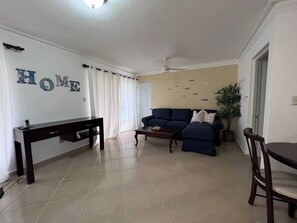 A living room with a sofa, a coffee table, a TV stand, and a dining area with a table and chairs. - Garden Condos 48 - Friendly 1BR APT, Sosua Center! (Sosúa)