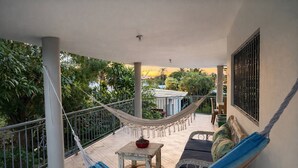 Un balcone con un'amaca, un tavolino con una pianta, un divano con cuscini e vista su spazi verdi e un edificio.