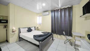 A hotel room with a bed, bedside tables, a desk, a chair, an air conditioning unit, and curtains. - Cheap Hotel Room in Sosua Center! (Sosúa)