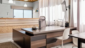 A modern office space with a wooden desk, white office chair, and a large window with curtains. - Centric Studio in Sosua Center Pool & Workspace (Sosúa)