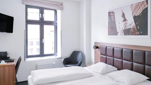 Ein Hotelzimmer mit Bett, Schreibtisch, Stuhl, Fenster und einem Bild an der Wand.