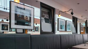 Ein Restaurantinnenraum mit schwarzen Ledersitzbänken, Holztischen und gerahmten Kunstwerken an den Wänden.
