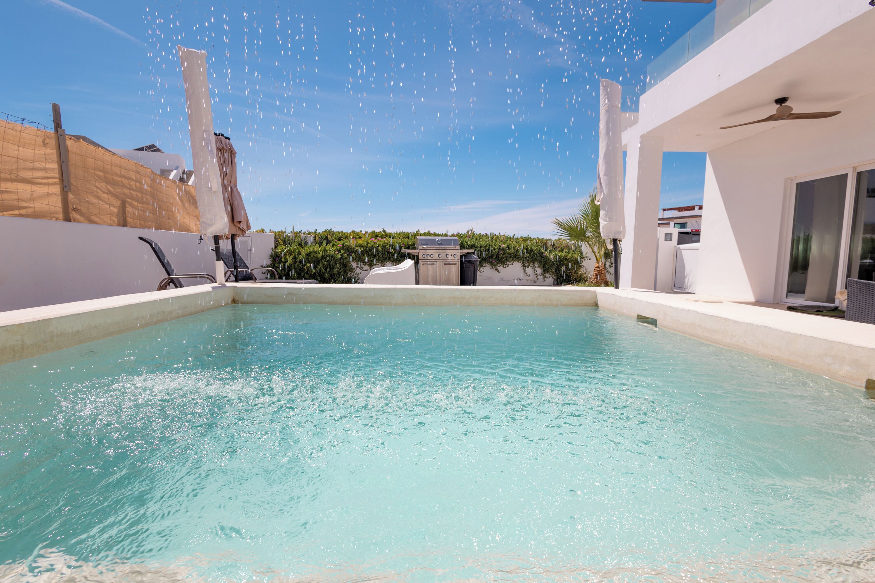 Ein Schwimmbecken unter blauem Himmel, umgeben von moderner Architektur und einer Grillgegend.