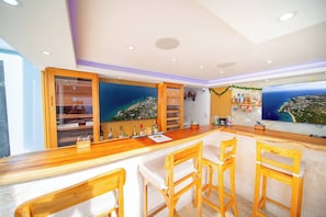 A bar area with wooden chairs, a counter, and a large TV screen displaying a scenic view. - Compai Unit 7 Home • AC, WiFi, Prime Location (Sosúa)