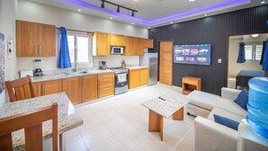 A modern kitchen with wooden cabinets, a microwave, stove, and a dining area with a table and chairs. - Compai Unit 7 Home • AC, WiFi, Prime Location (Sosúa)