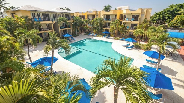 Een hotel met een zwembad, palmbomen en blauwe parasols.