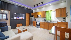 A modern kitchen with wooden cabinets, a microwave, and a coffee maker. There is a seating area with a sofa and a small table. - Casa de Compai Unit 8  AC, WiFi & Full Kitchen (Sosúa)