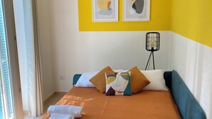 Ein Zimmer mit einem Bett, Kissen, einer Stehlampe und zwei gerahmten Kunstwerken an der Wand.