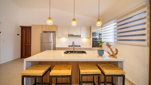 A modern kitchen with a central island, stainless steel appliances, and wooden stools. - 14 BR Getaway 2 mins from Sosua action! (Sosúa)