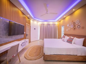 A modern bedroom with a flat-screen TV, a wooden desk, a bed with white bedding, and a ceiling fan. - 14 BR Getaway 2 mins from Sosua action! (Sosúa)