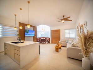 A modern living space with a kitchen, dining area, and a sofa. - 14 BR Getaway 2 mins from Sosua action! (Sosúa)