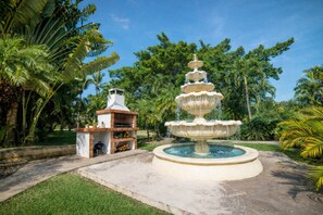 A multi-tiered fountain surrounded by lush greenery and a small barbecue area. - Garden Condos 35 Best Stylish apartment in Sosua (Sosúa)