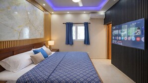 Una habitación de hotel con una cama grande, un ventilador de techo, un televisor montado en la pared y una ventana con cortinas.