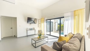 Ein modernes Wohnzimmer mit einer Couch, einem Couchtisch, einem Flachbildfernseher und einer Schiebetür zu einem Außenbereich.
