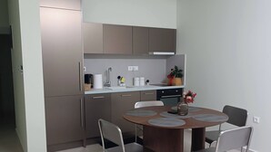 A modern kitchen with a dining area, featuring a round table with four chairs, a built-in oven, and a countertop with a sink. - Cozy Apartment in Nea Ionia Greece with Modern Amenities (Nea Ionia)