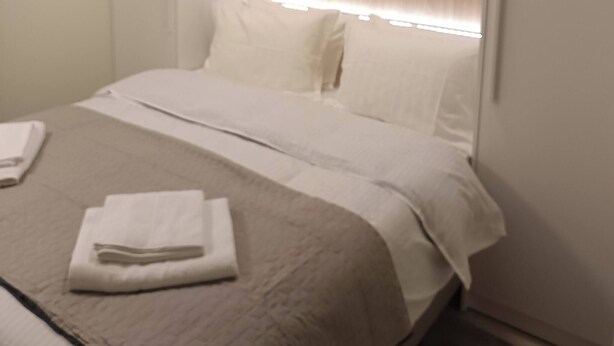 A hotel room with a bed, a wooden headboard, and a window with blinds. - Cozy Apartment in Nea Ionia Greece with Modern Amenities (Nea Ionia)