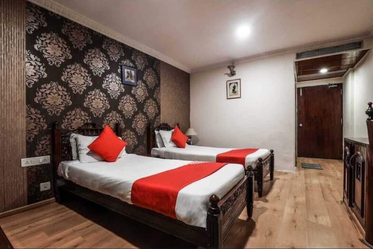 Habitació d'hotel amb dos llits, paper pintat amb dibuixos, terra de fusta i una porta.