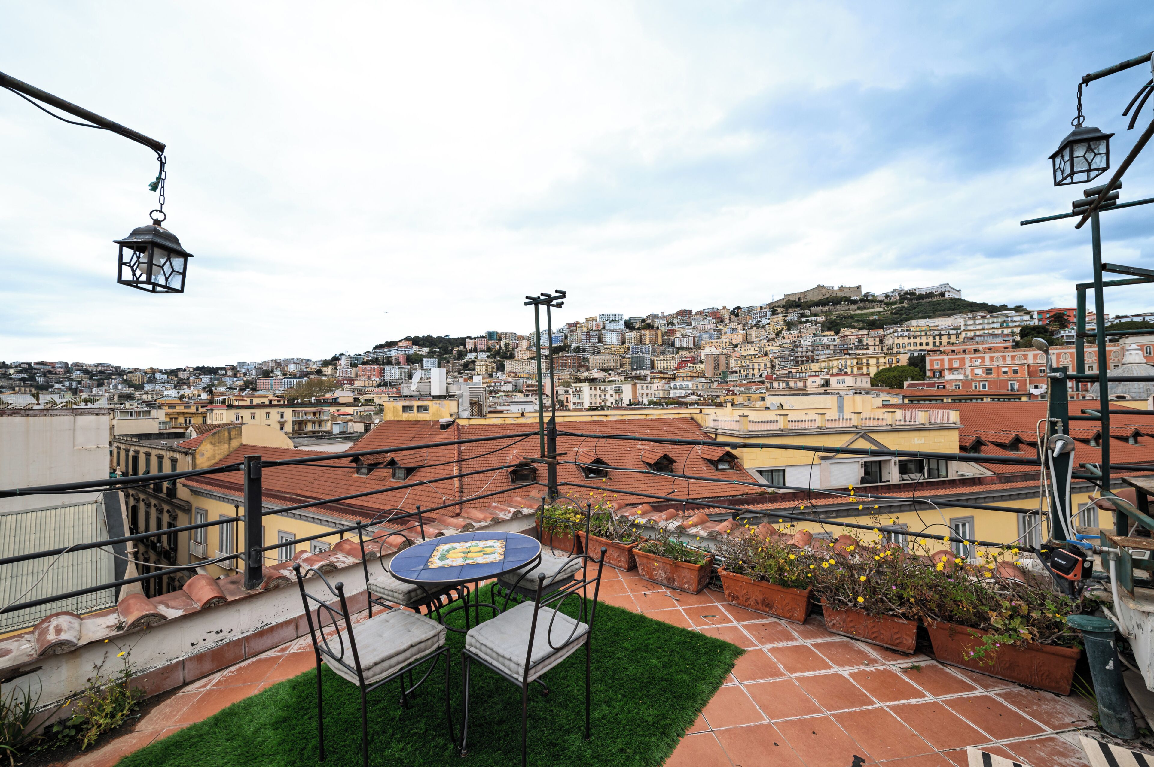 Eine Dachterrasse mit Tisch und Stühlen, Topfpflanzen und Blick auf eine dicht bebauete Stadtlandschaft.
