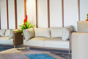 A modern living room with a beige sofa, a brown accent chair, and a patterned rug. - Vi Grand Inn (Sathyamangalam)