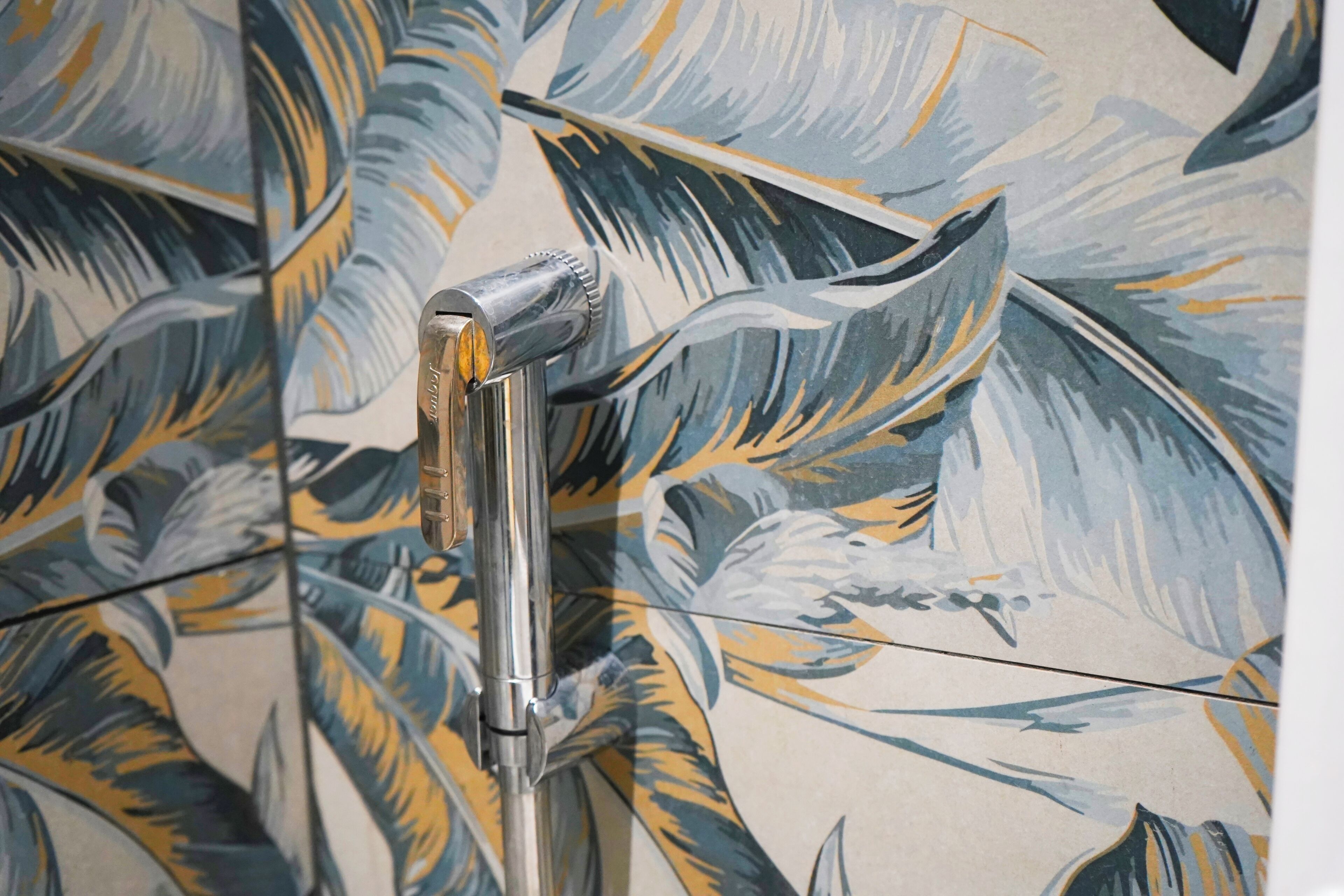 Eine Dusche mit modernem Wasserhahn und einer Wand mit tropischem Blattmuster.