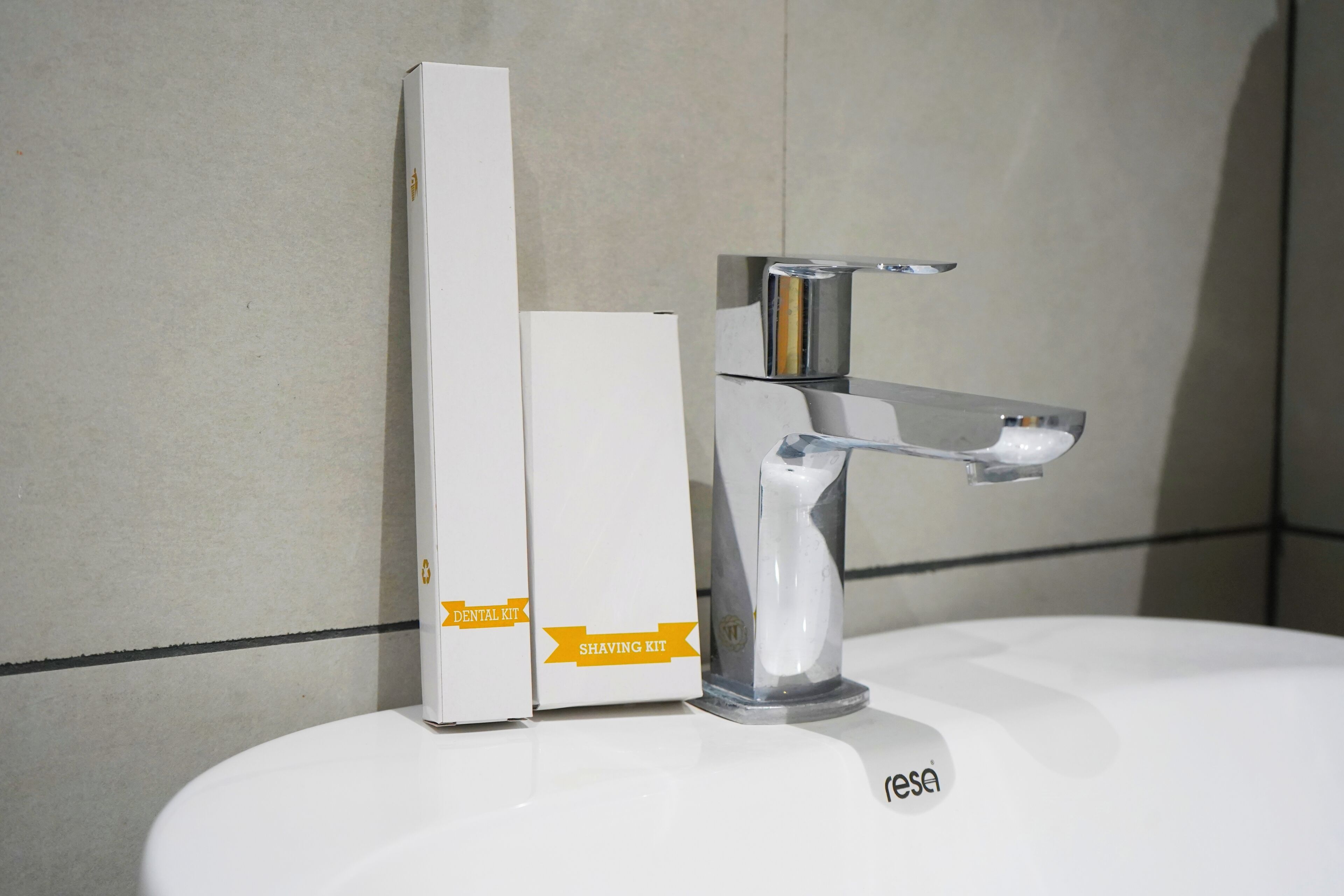 A bathroom sink with a chrome faucet and two white boxes labeled 'Dental Kit' and 'Shaving Kit' on the counter.