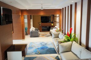 A modern living room with a sofa, a coffee table, a TV mounted on the wall, and a ceiling fan. - Vi Grand Inn (Sathyamangalam)
