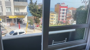 A room with a large window overlooking a street, a wooden table, and a chair. - Sinop kuzey pansiyon (Sinop)