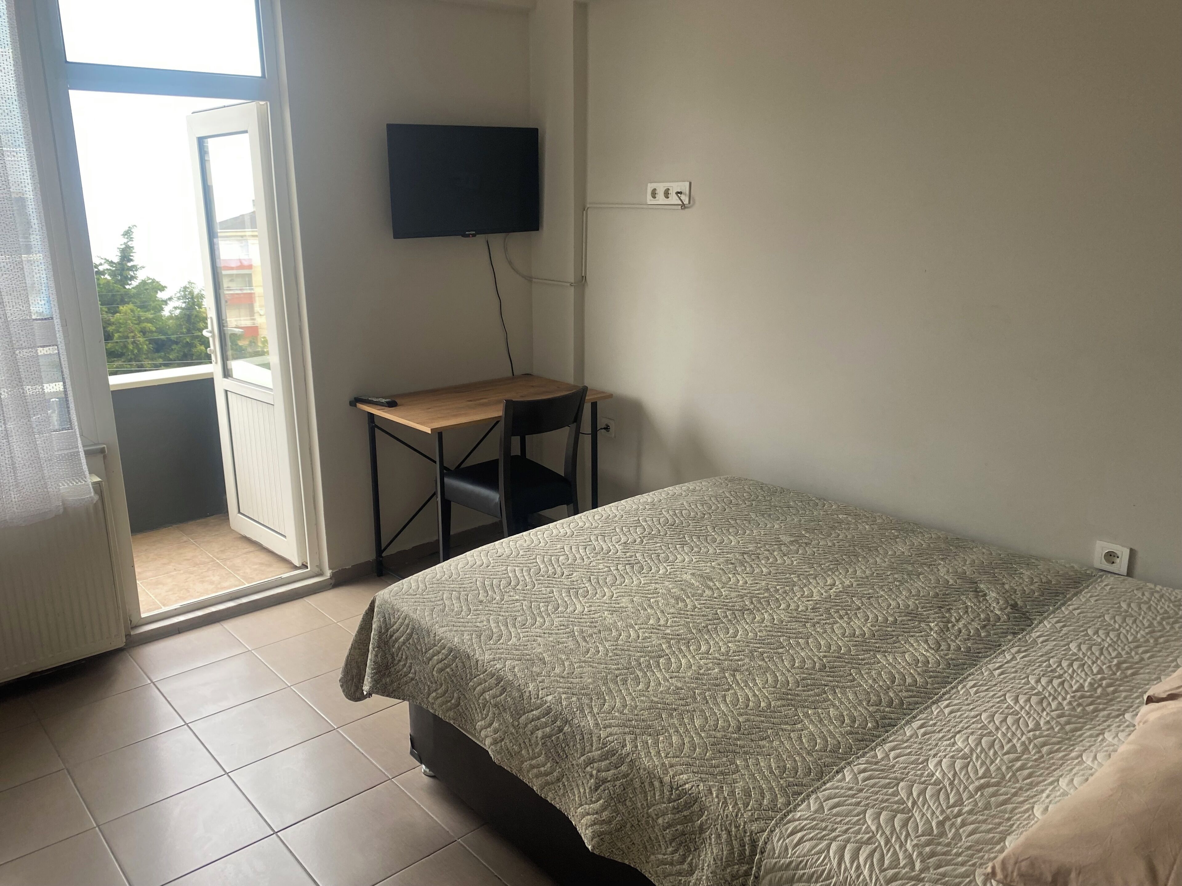 A bedroom with a bed, a desk, a chair, a television, and a balcony.