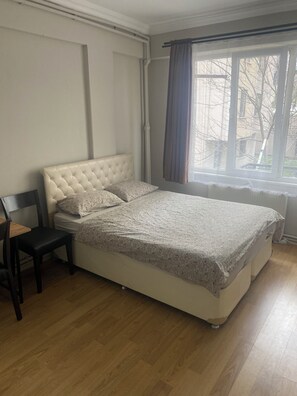 A bedroom with a tufted headboard, a bed with a patterned bedspread, a chair, and a window with curtains.