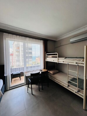 A room with a bunk bed, a small table with chairs, a window with sheer curtains, and an air conditioning unit on the wall.