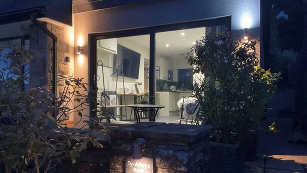 Una casa moderna con entrada de piedra, un área de comedor y una cocina visibles a través de puertas de vidrio.
