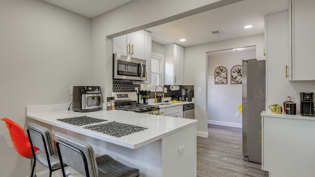A modern kitchen with white cabinetry, a central island, and a seating area with chairs. - 'The Red Door' Stylish Family Home in Falls Church (Falls Church)