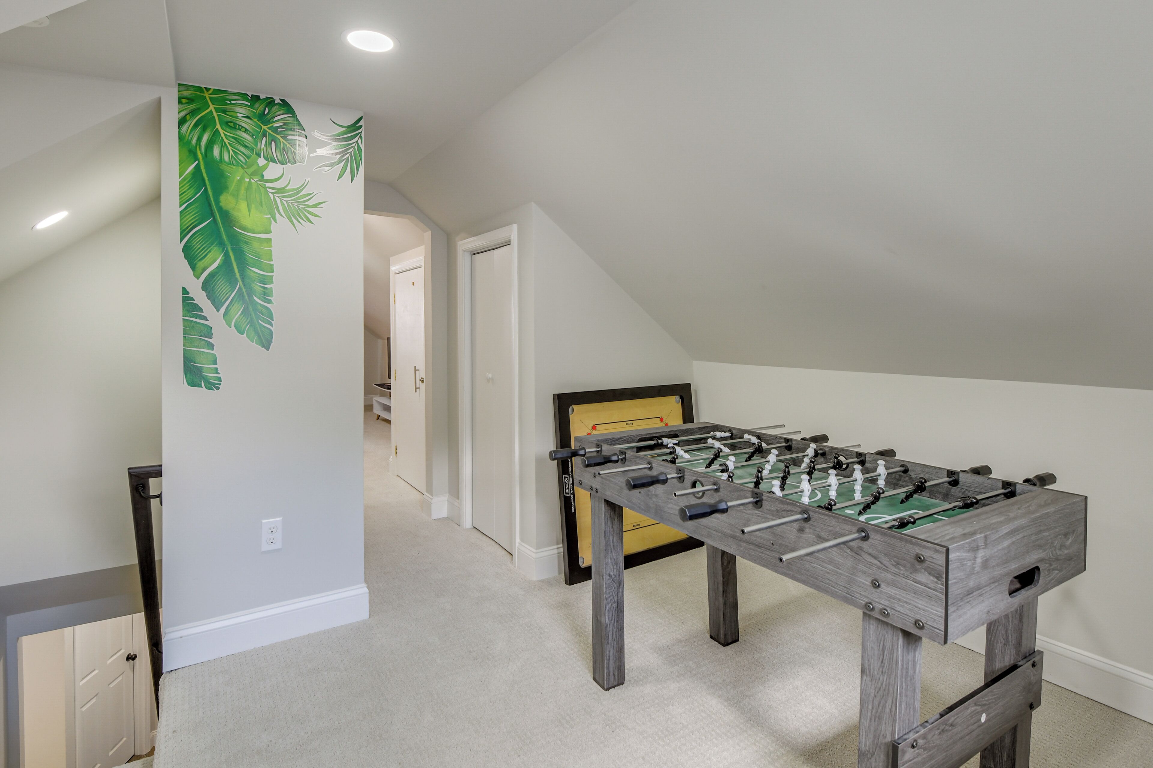 A room with a foosball table, a white door, and a hallway leading to another room.