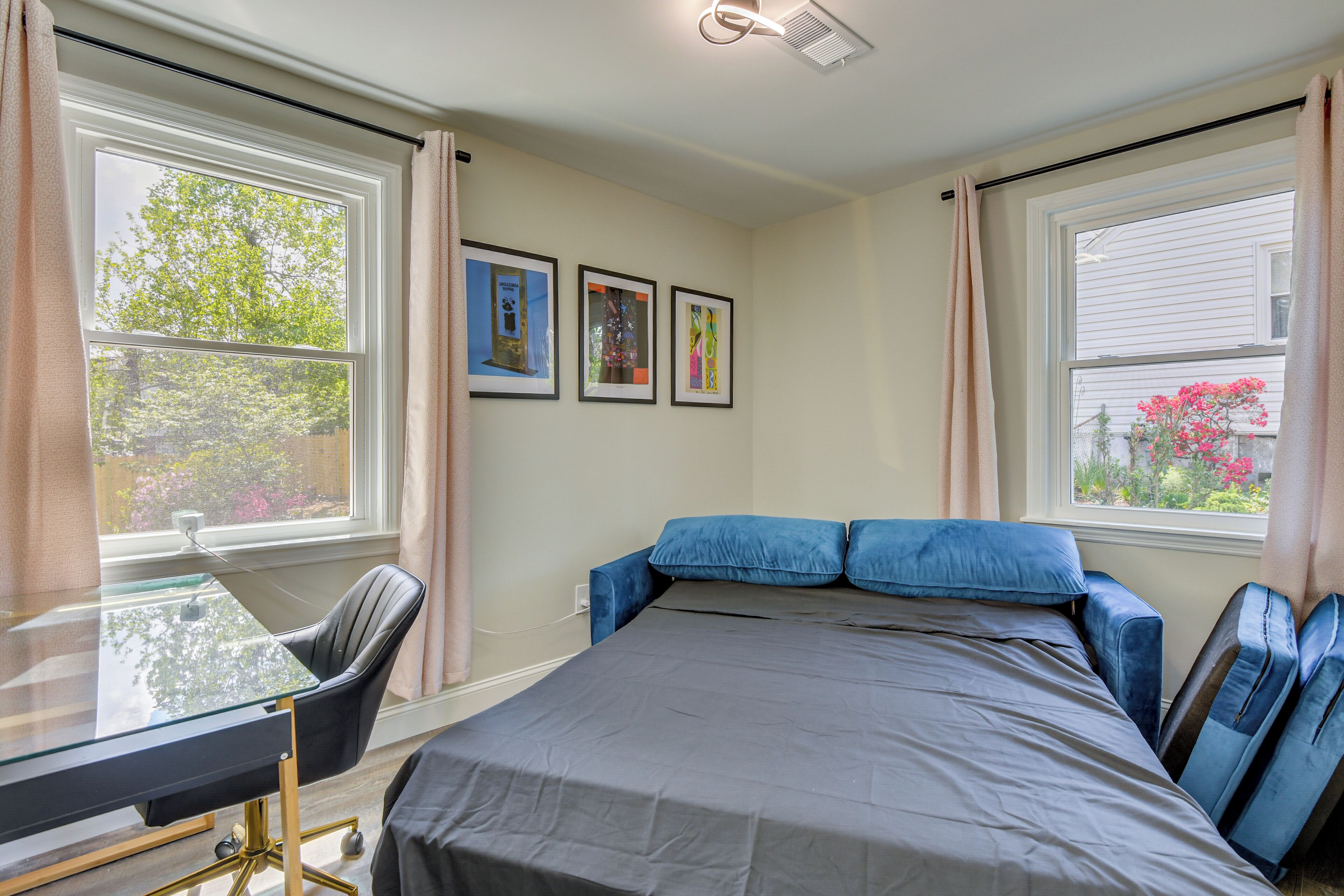 A bedroom with a bed, a desk, and two windows.