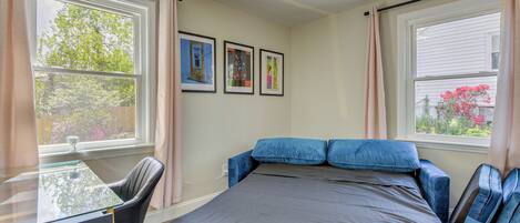 A bedroom with a bed, a desk, and two windows.