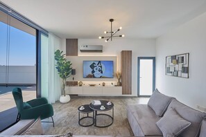A modern living room with a sofa, a green chair, a coffee table, and a TV. - Brand New 4 bedroom villa in Protaras center (Paralimni)