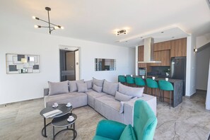 A modern living room with a sectional sofa, a coffee table, and a dining area with bar stools. - Brand New 4 bedroom villa in Protaras center (Paralimni)