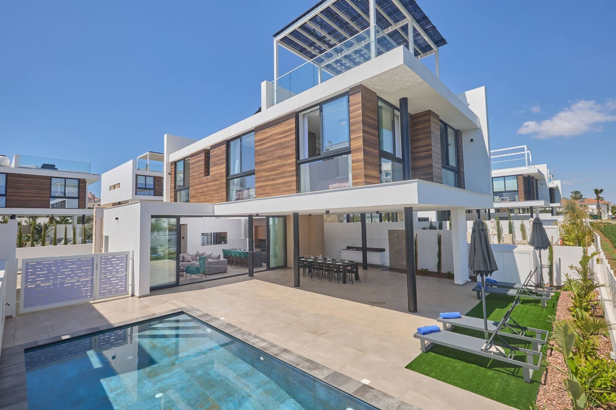 A modern two-story house with a swimming pool, outdoor seating, and a solar panel on the roof.