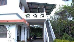 A two-story building with a covered entrance, potted plants, and a staircase leading to the upper level. - Kodai Blossom Cottages (Kodaikanal)