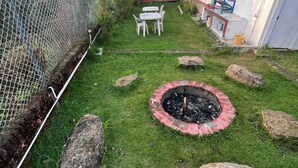 A well-maintained garden with a fire pit, large rocks, and a white table and chairs. - Kodai Blossom Cottages (Kodaikanal)