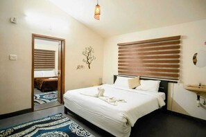 A hotel room with a bed, bedside table, mirror, window with blinds, and a wall-mounted sink. - Kodai Blossom Cottages (Kodaikanal)